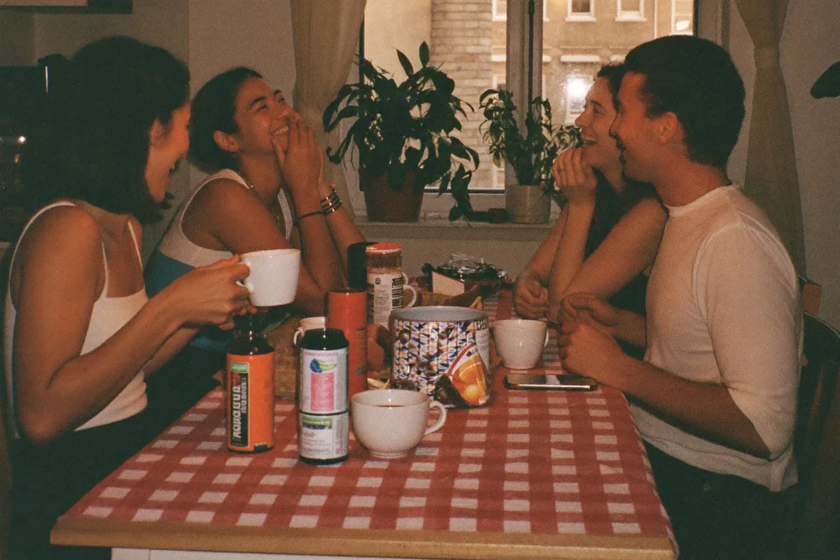 Four friends laughing around a kitchen table over coffee